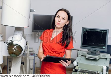 Close Up Portrait Of Young Caucasian Woman Doctor In Red Uniform, Holding Digital Tablet Pc, Posing 