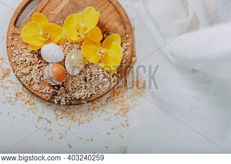 Three Easter Eggs With Yellow Orchid Flowers On Wooden Background With Sawdust Around. Easter Eggs W