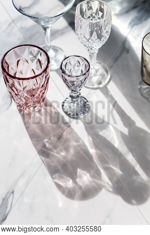 Variety Of Empty Glasses Diffrent Colors On Gray Stone Background With Hard Shadows And Sun Glare. O