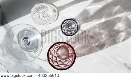 Variety Of Empty Glasses Diffrent Colors On Gray Stone Background With Hard Shadows And Sun Glare. O