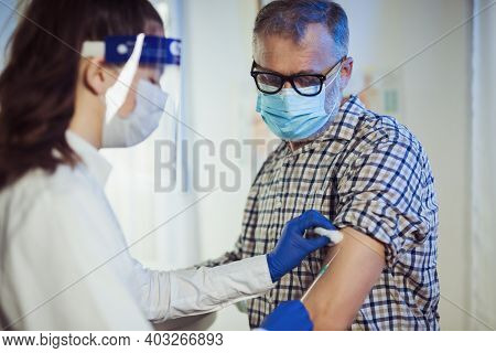 Young Woman Nurse With Surgical Mask And Face Shild Giving Injection To Senior Man. Covid-19 Or Coro