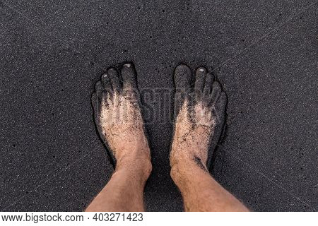 A Man Standing Barefoot On Volcanic Black Sand On The Tenerife Beach. Two Feet Covered By The Sand.