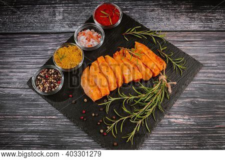 Chicken Fillet Thinly Sliced On A Black Ceramic Plate With Cooking Spices, Chili And Rosemary. Raw M