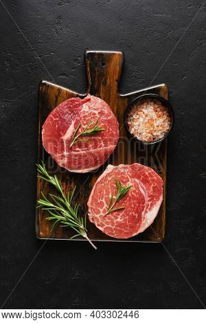 Two Fresh Parisienne Raw Steak On Wooden Board With Salt, Pepper And Rosmary In A Rustic Style On Ol