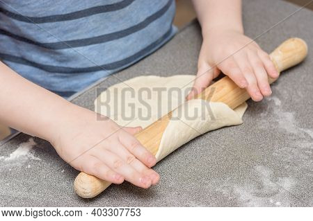 Close-up Of Children's Hands Using A Rolling Pin To Roll Out The Dough. Soft, Selective Focus. Conce