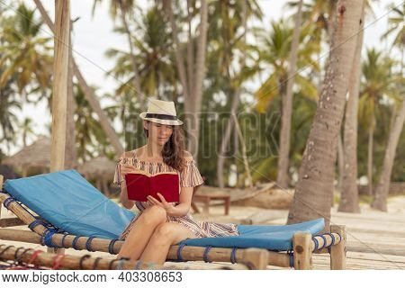 Young Woman Sitting On Sun Bed Underneath Palm Trees At Beautiful Tropical Island Exotic Beach Resor