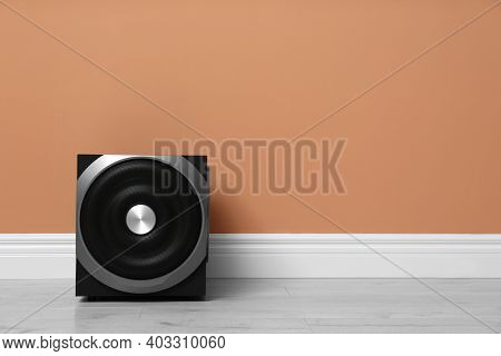 Modern Powerful Subwoofer On Floor Near Orange Wall, Space For Text. Audio Speaker System
