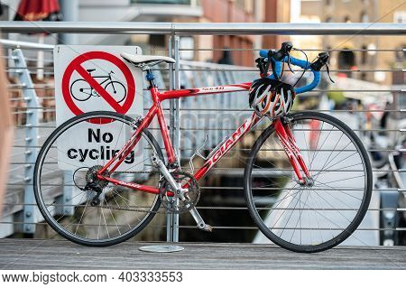London, Uk - November 2, 2020: Red Bike Leaning Against A No Cycling Sign On Metal Railings.