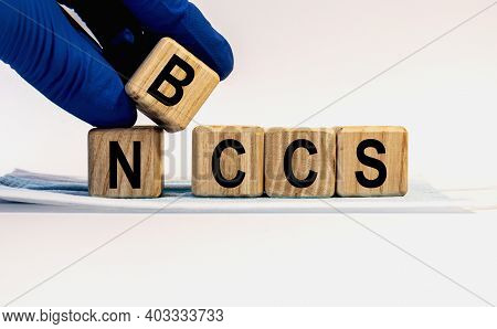 Text Nbccs Made From Wooden Cubes. Hands In A Blue Glove.