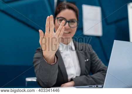 Business Woman Saying Hello In Vulcan Style While Sitting At Her Desk In The Office.