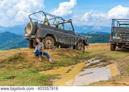 Jeeping Car Mountain Travel. Beautiful Girl Rest Next Dirty Jeep And Big Puddle Of Mudd. Carpathian 