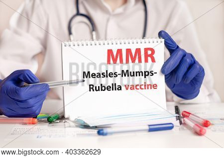 Mmr Card In Hands Of Medical Doctor. Doctor's Hands In Blue Gloves Holding A Sheet Of Paper With Tex