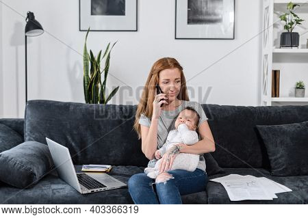 Freelancer Mom Works From Home With A Newborn Baby Girl On Hands. A Working Mother Is Using Laptop W