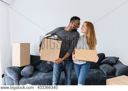 Cheerful Young Multiracial Couple In Love Moves To New House, Diverse Couple Stands And Holds The Ca
