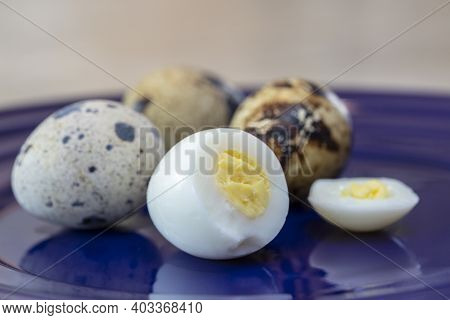 Quail Eggs On A Plate, With One Egg Shelled, Hard Boiled And Yolk Exposed, And Three Spotted Whole E