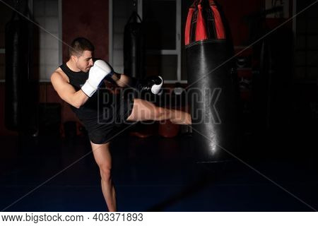 Muscular Handsome Kickboxing Fighter Giving A Forceful Kick During A Practise Round With A Boxing Ba