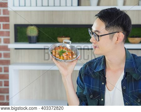 Young Man Wearing Glasses Sitting Looking At The Fried Egg Served On A Pan With Colorful Toppings Se