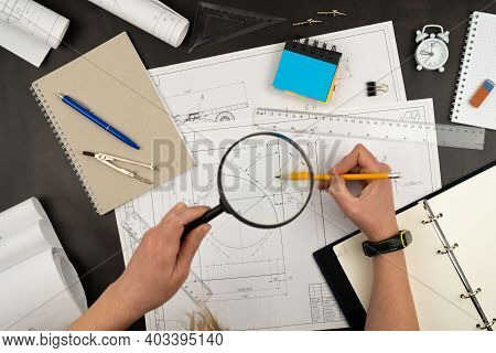 Look Through A Magnifying Glass. Mechanical Drawing On Sheets Of Paper. Hands On The Table Top View.