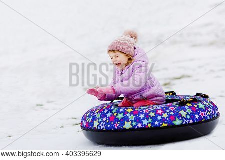 Active Toddler Girl Sliding Down The Hill On Snow Tube. Cute Little Happy Child Having Fun Outdoors 