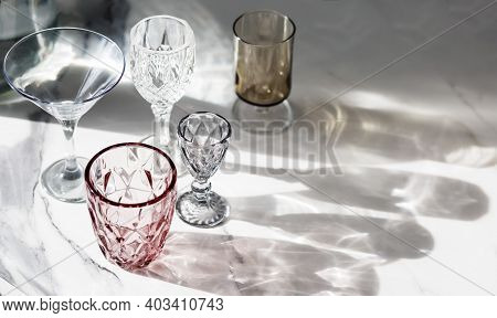 Variety Of Empty Glasses Diffrent Colors On Gray Stone Background With Hard Shadows And Sun Glare. O