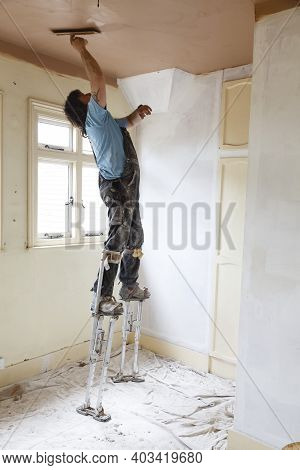 Buckingham, Uk - May 07, 2015. A Plasterer Skims A High Ceiling Whilst Standing On Stilts. A Skilled