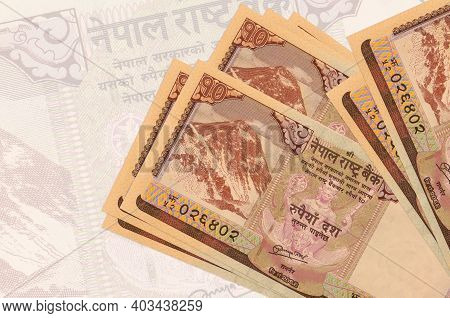 10 Nepalese Rupees Bills Lies In Stack On Background Of Big Semi-transparent Banknote. Abstract Pres