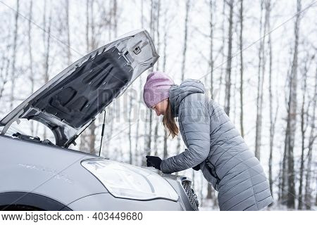 Car Repair On The Road In Winter. Young Girl Is Trying To Fix A Car Breakdown Under The Soot On The 