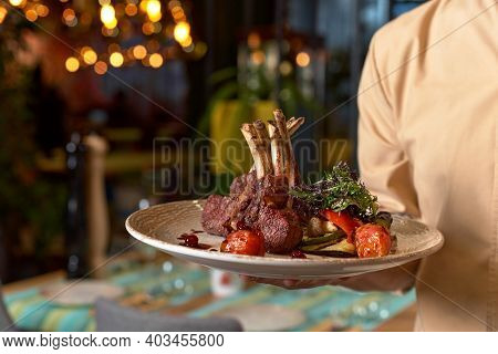 Hands Holding Cooked Tomahawk Long Bone Ribeye Steak On A Plate In Restaurant At The Waitress's Hand