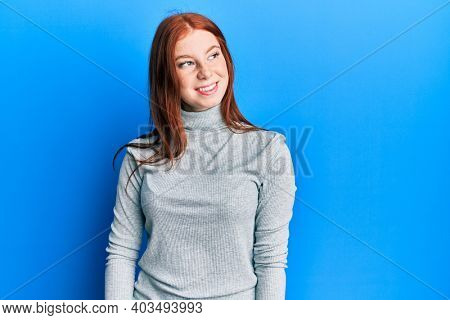 Young red head girl wearing turtleneck sweater looking to side, relax profile pose with natural face and confident smile. 