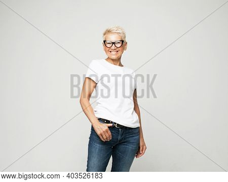 Aged people, lifestyle and maturity concept: blonde fifty year old European female with stylish pixie haircut and eyeglasses smiling at camera and posing isolated over grey background.