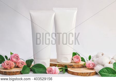 White Unbranded Tubes For Cosmetics With Wood Cuts, Small Pink Roses And Cotton Flowers On White Bac