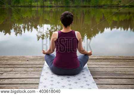 Young Short-haired Woman Meditating By A Lake.