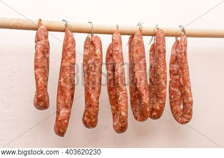 Drying Sausages From Raw Minced Meat In Limbo On A Wooden Stick On A White Wall Background At Home.