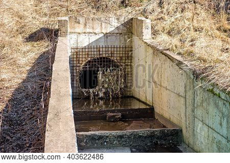 Storm Sewer Pipe Closed With Grating. Broken Sewer Entrance. Plastic Debris Stuck On The Drain Grate