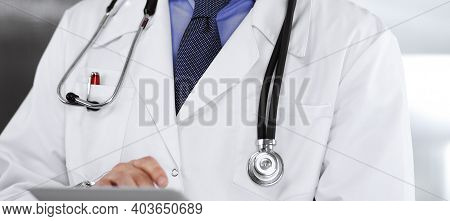Unknown Male Doctor Iusing Tablet Computer In His Hands, While Standing In Clinic. Medicine Concept 