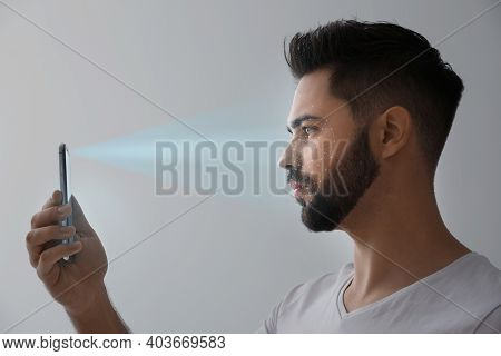 Young Man Unlocking Smartphone With Facial Scanner On Grey Background. Biometric Verification