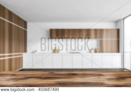 Wooden Desk On Blurred Background Of White And Wooden Empty Kitchen Set With Window And Parquet Floo