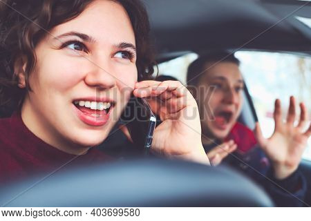 Happy Curly Haired Girl Talking On Mobile Phone While Driving Car. Man In Next Seat Is Terrified Of 
