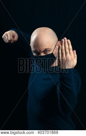 Portrait Of A Bald Man In A Black Medical Mask On A Dark Background. A Man In A Belligerent Stance I