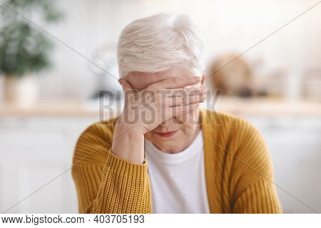 Senior Grey-haired Woman Suffering From Migraine, Touching Her Forehead, Kitchen Interior, Closeup. 