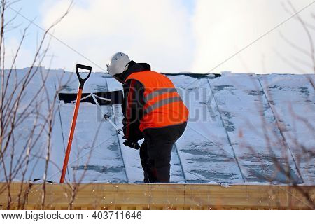 Worker Removing Snow On The Roof Of A Building. Snow Removal, Climber Cleaning Roof In Winter