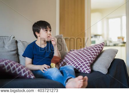 Portrait New Normal Lifestyle Kid Siting On Sofa Eating Potato Crisps While Watching Tv, Young Boy E
