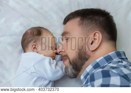Happy Bearded Middle-aged Father With Newborn Baby Lying In Bed Face To Face, The Concept Of Fatherh