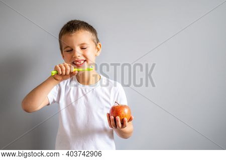 Boy Without Milk Upper Tooth In White T-shirt Smiling And Holding An Apple And Toothbrush In Hands O