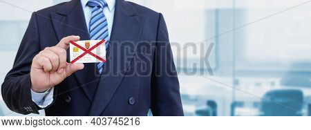 Cropped Image Of Businessman Holding Plastic Credit Card With Printed Flag Of Jersey. Background Blu