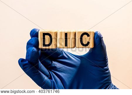 The Word Dic Which Is Made From Wooden Cubes. Hands In A Blue Glove. Isolated On White Background.