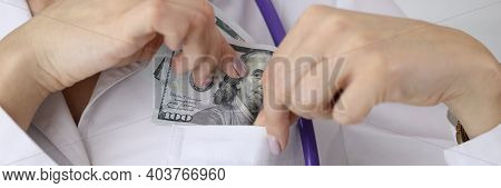 Doctor Puting Dollar Bill In Uniform Pocket At Clinic Closeup. Corruption In Medicine Concept