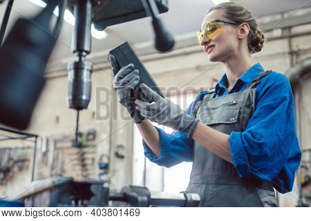 Woman in metal workshop checking workpiece for accuracy