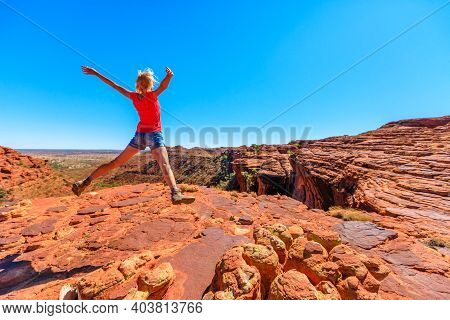 Young Hiking Girl Jumping At Kings Canyon. Enjoying In Red Center Outback. Jumper Among Sandstone Fo