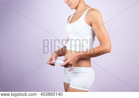 Young Caucasian Woman In White T-shirt And Shorts, Holding Pregnancy Test On Neutral Background. Wom
